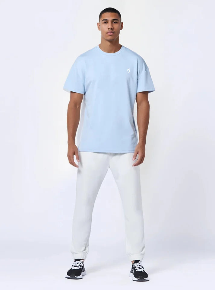Front full photo of a model wearing radowl strength heavyweight oversized gym tshirt ice blue colour  this t-shirt made form heavy terry which keeps you warm during winters and this tshirt have Radowl logo which make it a best gym wear tee.