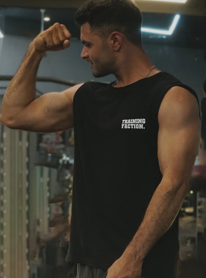 Male gym athlete flexing in a black sleeveless gym vest with Training Faction print inside a gym. Designed for airflow and performance by Radowl, this product is the 'Training Faction Black Gym Vest.'