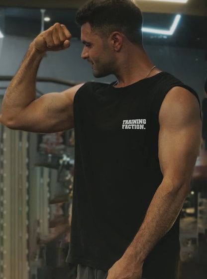 Male gym athlete flexing in a black sleeveless gym vest with Training Faction print inside a gym. Designed for airflow and performance by Radowl, this product is the 'Training Faction Black Gym Vest.'